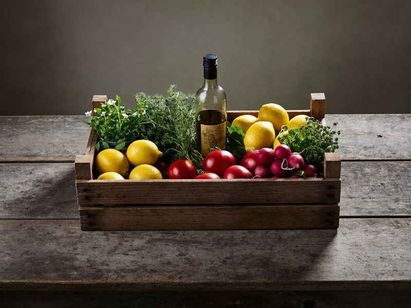 Cassetta di verdure di stagione, erbe, limoni e olio su piano rustico